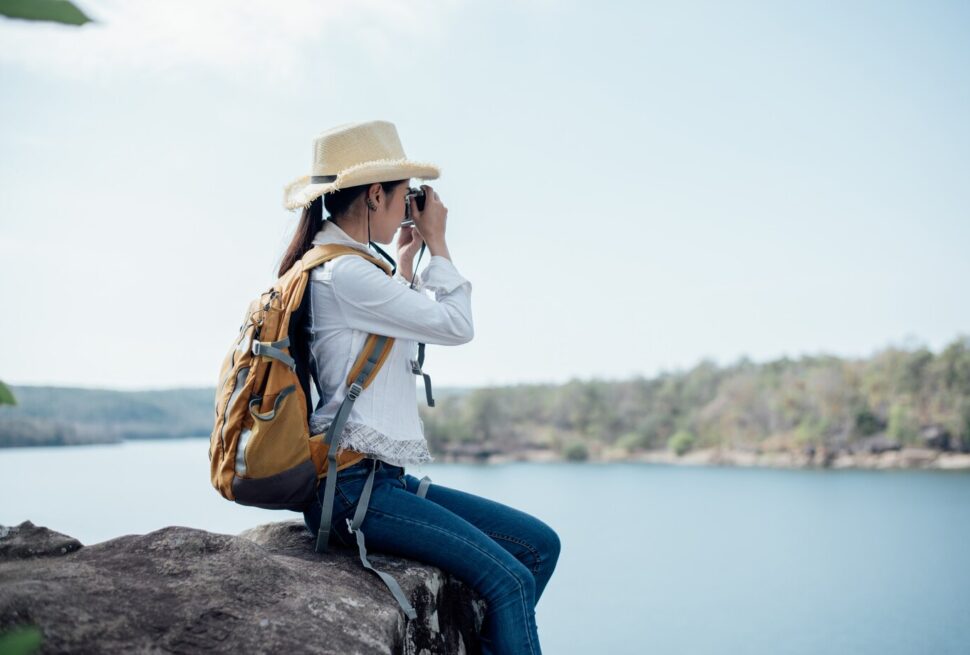a woman sitting on a rock taking a picture of a lake