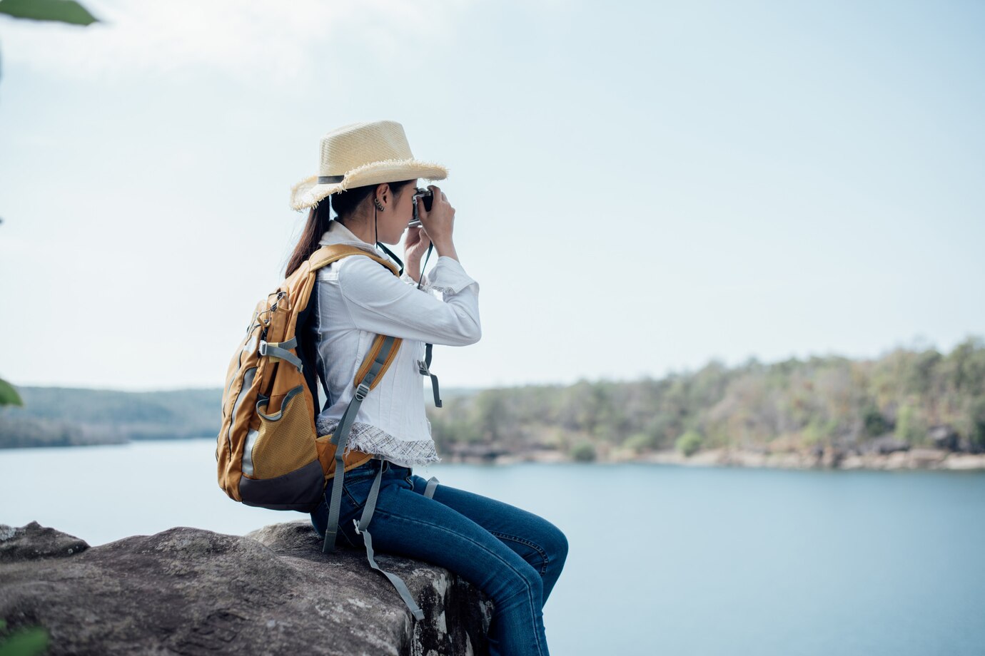 a woman sitting on a rock taking a picture of a lake
